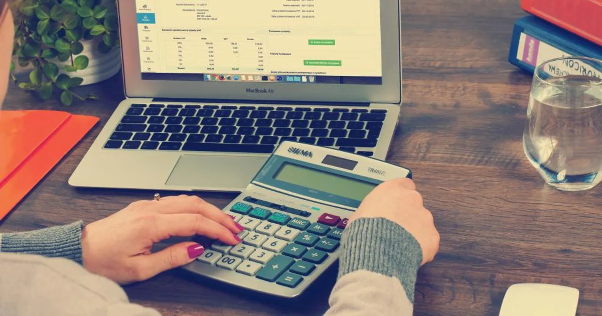 An accounts payable desk with invoice software open and a calculator in use